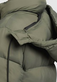 Giacca imbottita verde oliva con texture trapuntata, dotata di chiusura con zip nera e collo alto per una maggiore isolamento.