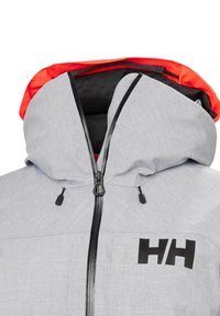 Šedá zateplená bunda s výrazn�ým černým zipem a kapucí; vnitřek má živé oranžové podšívku; obsahuje texturovaný vzor a potisknuté logo.