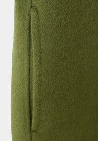 Gros plan sur un tissu en laine vert olive montrant une poche passepoil verticale avec des coutures soignées.