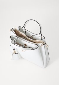 Borsa bianca con bordi neri, doppi manici superiori, chiusura con zip e un piccolo tag removibile. Esterno testurizzato e fodera interna beige.
