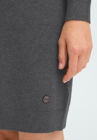 Grå stickad klänning med ribbad textur. Har en rundad halsringning, långa ärmar och en liten logotypknapp nära fållen.