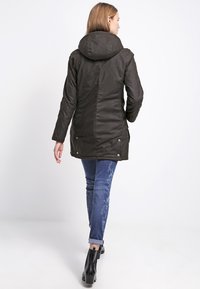 Dark green parka jacket with a hood, featuring a buttoned front and side pockets, paired with blue patterned jeans and black ankle boots.