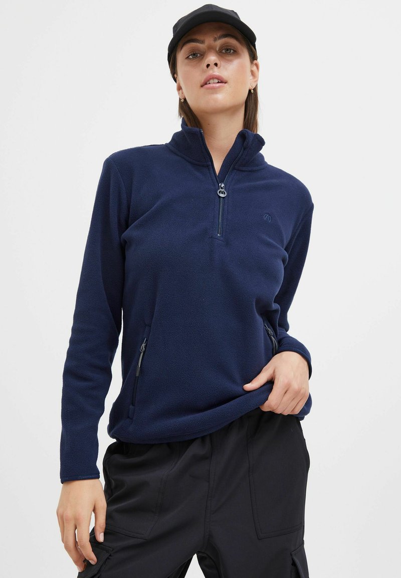 Pull-over en polaire bleu marine avec un col zippé mi-hauteur, des poches latérales et une texture douce. Présente un logo sur la poitrine et des manches longues.