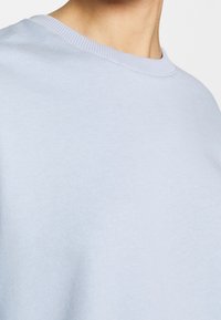 Felpa azzurra con scollo rotondo, realizzata in tessuto morbido, con una superficie liscia e un design minimalista.