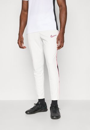 Hvite sportsbukser med rosa sidestriper, kombinert med en hvit og svart kortermet topp, og svarte sportsko.