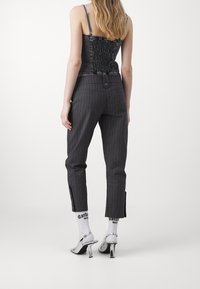 Top corto nero a costine con spalline regolabili, abbinato a pantaloni grigi a righe con fessure laterali e dettagli in bottone, e tacchi argentati.