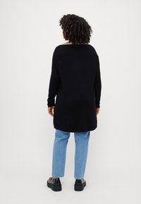 Black long-sleeve tunic sweater with a relaxed fit, featuring a round neckline. Paired with light blue straight-leg jeans and black platform shoes.