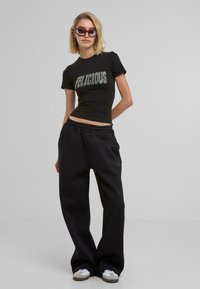 Svart åtsittande t-shirt med texten "FELICIOUS" i silver, parat med lösa svarta sweatpants, utförda i ett mjukt material och med elastisk midja.
