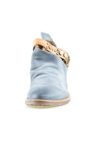 Bottine en daim bleu avec une sangle en cuir beige ornée de clous métalliques, vue de face sur fond blanc.