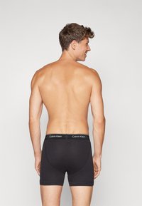 Crni pamučni bokserice s mekanim pojasom na kojem se nalazi logotip Calvin Klein, prikazane na muškom modelu s leđa.