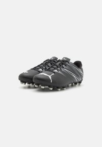 Botas de fútbol negras con una parte superior sintética suave, con acentos de rayas blancas y tacos moldeados para tracción. Logo mostrado en el costado.