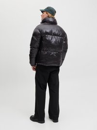 Jachetă puffer din material negru lucios, având un guler înalt și un design cu quilt horizontal. Asortată cu pantaloni negri largi și pantofi negri.