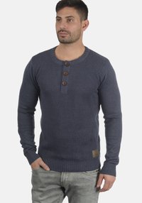 Maglione lavorato a maglia blu navy con scollatura a girocollo, tre bottoni in legno, polsini a coste e una finitura testurizzata. Include una piccola etichetta con il marchio.