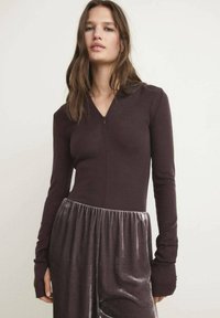 Body a maniche lunghe in tessuto marrone scuro con scollatura a V e chiusura con zip. La parte inferiore è in morbido velluto plissettato di colore grigio chiaro.