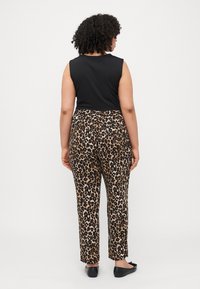 Schwarzes ärmelloses Oberteil kombiniert mit hoch taillierten Hose im Leopardenmuster mit beigem Hintergrund und dunklen Flecken. Es werden flache schwarze Schuhe getragen.