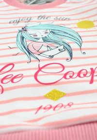 Fille aux longs cheveux turquoise tenant un bateau en papier, soleil, oiseaux, et fond rayé avec le texte "profite du soleil" et "Lee Cooper 1908".