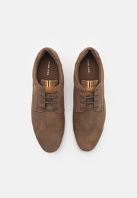 Zapatos de algodón marrón con acentos de cuero, punta redonda, diseño de cordones y una etiqueta a rayas en contraste en la lengüeta. Suela de goma.