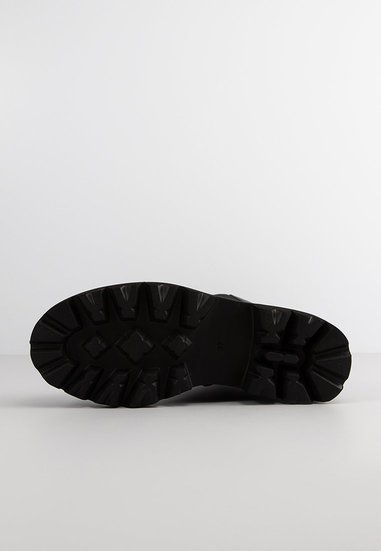 Schwarze Gummibootsohle mit einem robusten, strukturierten Profilmuster und tiefen Rillen für Traktion und Haltbarkeit. Klare Größenmarkierungen sind sichtbar.