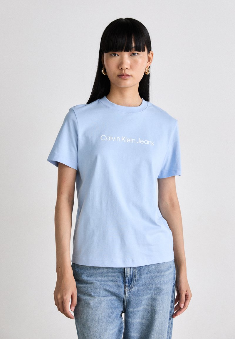 Světle modré bavlněné tričko s krátkým rukávem, s bílým logem "Calvin Klein Jeans" na hrudi. Ležérní střih, hladká textura.