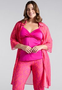 Completo rosa brillante composto da un top aderente e un kimono leggero e trasparente. I pantaloni presentano un motivo a foglia in una tonalità di rosa a contrasto.
