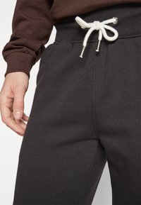 Dunkelgraue Jogginghosen mit weicher Textur, ausgestattet mit einem Kordelzugbund aus weißem Kordel und metallenen Enden, dezenten Nähdetails.