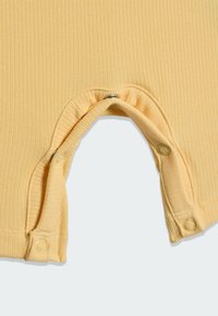 Žlutý žebrovaný overal s patentkami na spodní straně, měkkou texturou a zaoblenými otvory na nohách pro snadné oblékání.