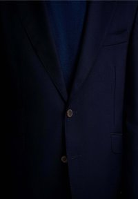 Blazer azul marino con un tejido texturizado, dos bolsillos frontales, un cierre con un solo botón marrón y diseño de solapa de muesca.