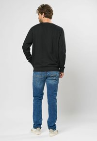 Zwarte sweatshirt met lange mouwen, ronde hals en geribde manchetten, gecombineerd met lichtblauwe denim jeans en lichtgekleurde sneakers.