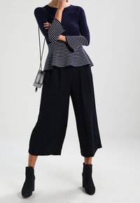 Haut péplum en maille bleu marine avec manches rayées, associé à un pantalon large noir et des bottines à talons. Sac bandoulière simple inclus.