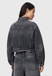 Chaqueta de mezclilla negra cortada con dobladillo deshilachado, puños abotonados y bolsillos con parche. Textura suave con un ajuste relajado y un diseño minimalista.