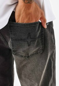 Zwarte spijkerbroek van denim met een achterzak voorzien van een kruissteekpatroon, een soepele textuur en een rechte pijp.