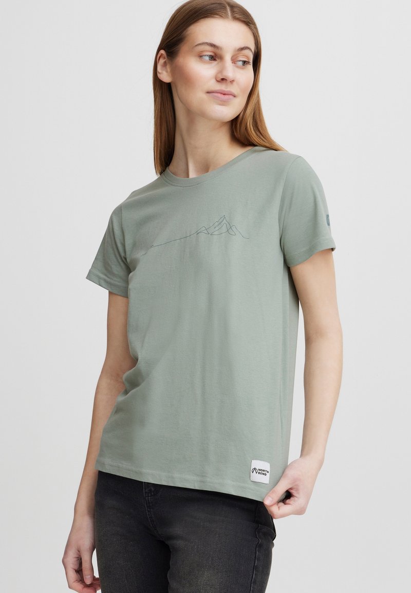 Camiseta de algodón verde claro con mangas cortas, que presenta un gráfico de contorno de montaña en azul oscuro y una pequeña etiqueta de la marca en el dobladillo.