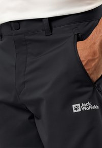 Schwarze Outdoor-Hosen aus glattem, leichtem Material. Mit Reißverschlusstasche und Logo auf der Vorderseite. Taillierte Passform mit klassischem Bund.