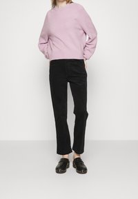 Pull violet clair en tricot, pantalon en velours côtelé noir et sabots noirs cloutés, présentés sur un fond blanc uni.