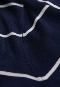 Nahaufnahme eines marineblauen Strickstoffs mit weißen horizontalen Streifen und sichtbaren Nahtnähten.