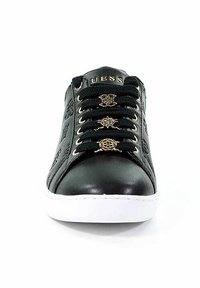 Baskets en cuir noir avec semelle blanche, lacets noirs passés à travers des œillets dorés, et charms décoratifs dorés sur les lacets.