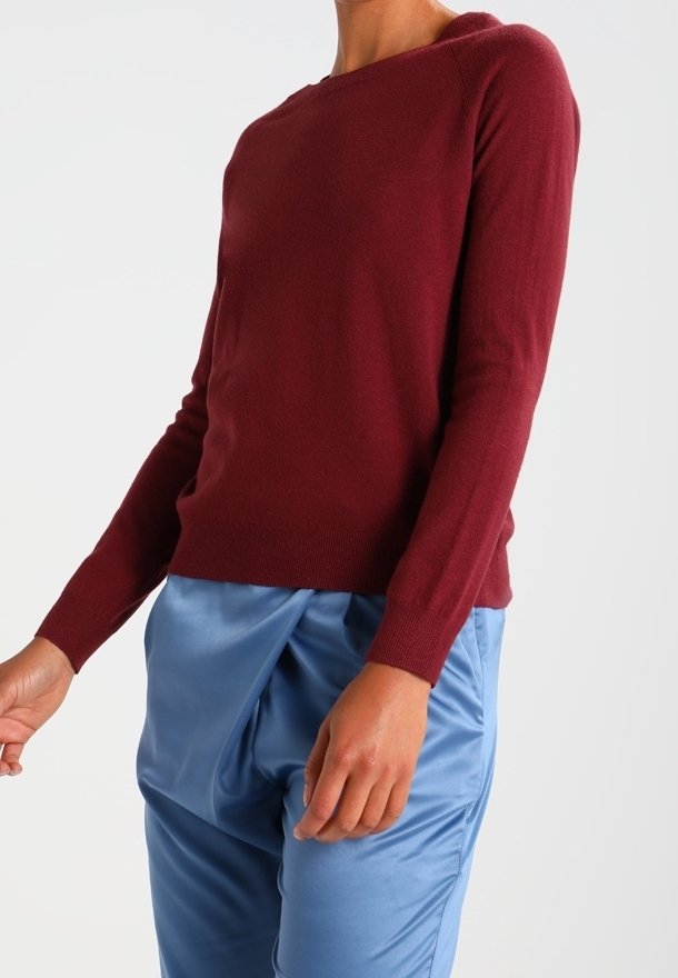 Pull en maille ajusté couleur bordeaux avec un large col rond et des manches longues, associé à un pantalon bleu clair drapé. Texture lisse.