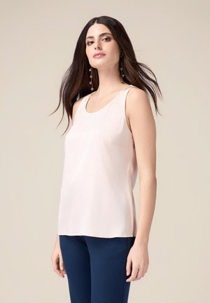 Haut sans manches rose clair en tissu lisse, avec un col rond et une coupe décontractée, associé à un pantalon bleu marine.