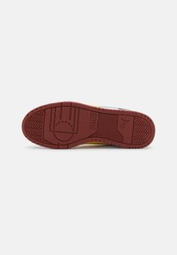 Red rubber outsoles with textured patterns; features a circular logo and side accents in yellow and black for contrast.
