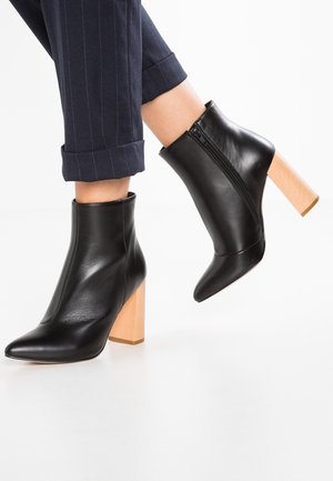 Černé kožené kotníkové boty s špičatou špičkou, vybavené viditelným bočním zipem a robustním dřevěným podpatkem. Texturovaný povrch a elegantní design.