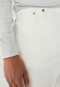 Jeans de mezclilla blanca de corte slim, con bolsillos frontales, herrajes metálicos en contraste y detalles de costura visibles. Textura suave.