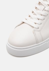 Baskets en cuir blanc avec lacets plats blancs, bout arrondi et semelle en caoutchouc texturé. Détails cousus le long des côtés.