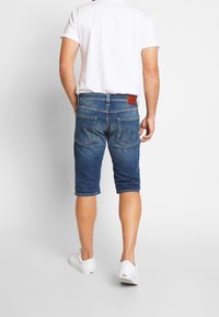 Denimshorts i medelblått med en urtvättad finish, knälängd, med två bakfickor och en brun läderlapp på midjan.