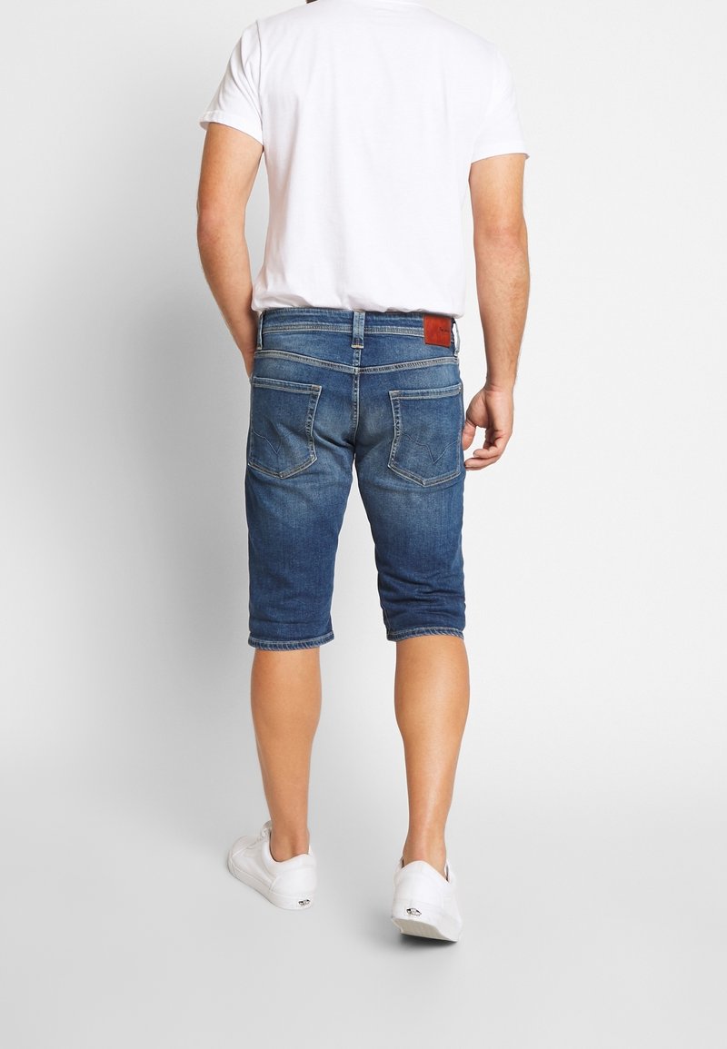 Denimshorts i medelblått med en urtvättad finish, knälängd, med två bakfickor och en brun läderlapp på midjan.