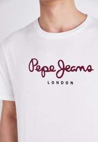 Hvit bomulls T-skjorte med maroon "Pepe Jeans" logo og svart "LONDON" tekst. Rund hals, korte ermer, glatt tekstur.