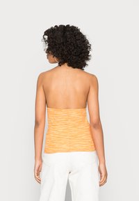 Top laranja sem alças, em tecido texturizado, com design canelado e formato ajustado. Usado com calças de cintura alta de cor clara.