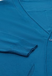 Türkiz kötött kardigán V-nyakkal, bordás mandzsettával és gombos záródással. Puha tapintás, enyhén szabott fazon és minimális részletezés.