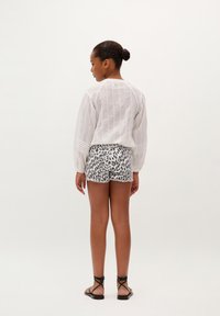 Camiseta blanca de manga larga con rayas texturizadas, combinada con un short de leopardo en blanco y negro. La modelo lleva sandalias negras con tiras.