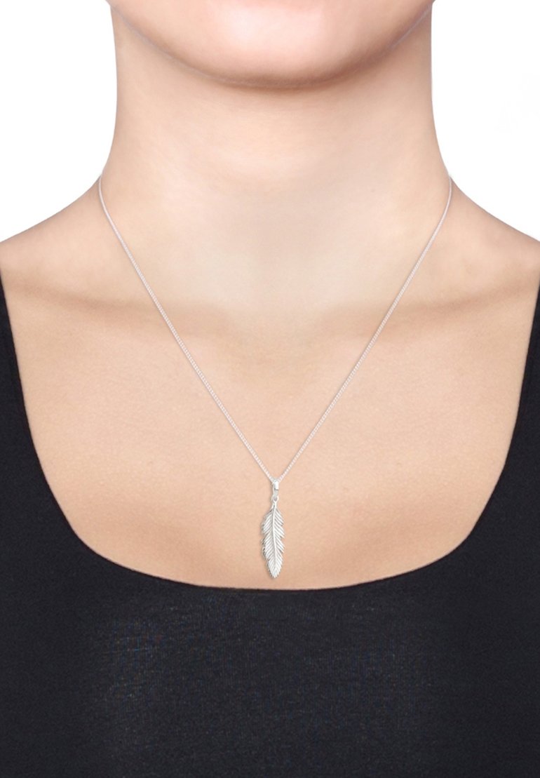 Silberner Federanhänger an einer dünnen Kette, mit detaillierter Federstruktur, getragen auf nackter Haut mit einem schwarzen Oberteil.