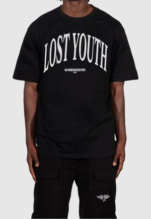 Osoba nosząca czarną koszulkę z dużymi białymi literami „LOST YOUTH” oraz spodnie bojówki z pasującym logo „Lost Youth” na kieszeni.